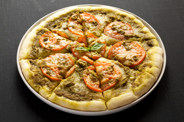Homemade Pesto Pizza with Fresh Tomatoes and Mozzarella on a black background, low angle view.
