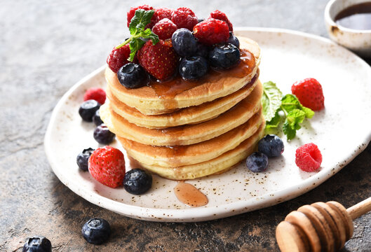 Pancakes with berries and maple syrup for breakfast on a dark concrete background.