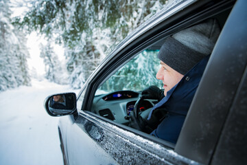 Fototapeta na wymiar Man in warm winter clothes sitting in car. Snowy winter country road, car covered with ice, Beautiful forest under the snow. 