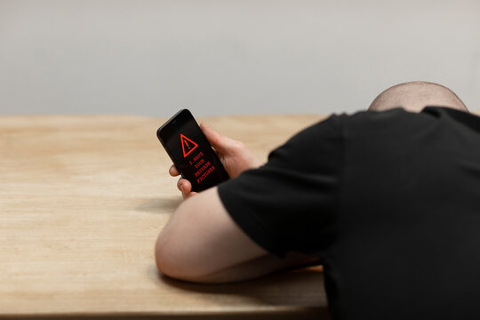 A red warning text saying &lsquo;I have your private pictures&rsquo; on a cell phone. A man, the sextortion victim holding his phone while being desperate. Cybercrime
