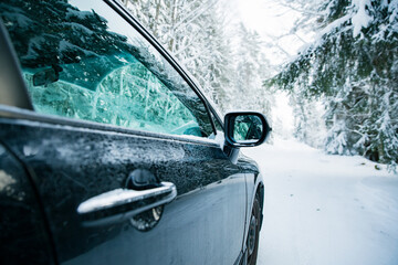 Car covered with snow and ice driving on the winter road. Beautiful landscape of winter forest and snowy country side. 