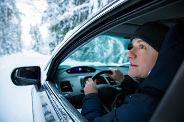 Man in warm winter clothes sitting in car. Snowy winter country road, car covered with ice, Beautiful forest under the snow. 