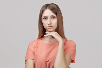 Pensive blond girl with thoughtful expression, keeps hand on chin, plans something or makes choice