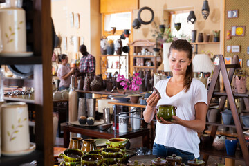 Young positive woman choosing ceramic products in pottery store