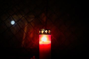 Burning candle in front of a metallic net during the night.