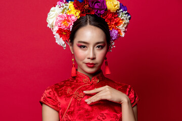 Fototapeta premium Gorgeous Asian woman in traditional Cheongsam dress with colorful make up and flower wreath on head in red isolated studio background