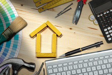 Small wooden house made of toy blocks on the desk, with work tools, computer keyboard, calculator and Euro coins. Home improvement concept.