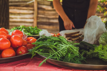 Fresh clean tomatoes, arugula and lettuce on large metal plates. Concept of cooking in the backyard on a sunny summer day. Preparing for barbecue with neighbors. catering in nature