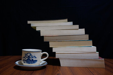 Piles of books and cup of coffee over black background