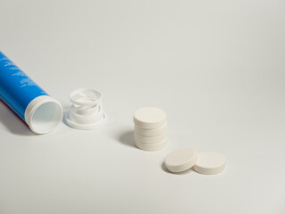 A round white pills and open a blue plastic tube on the light background