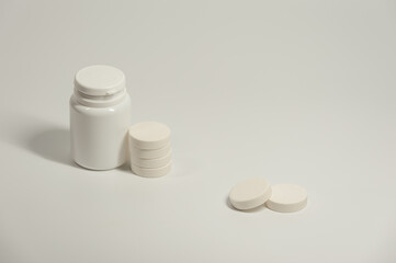 A round white pills and plastic container on the light background