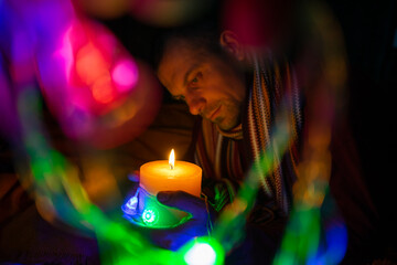 The man looks at the burning candle. Bokeh is around