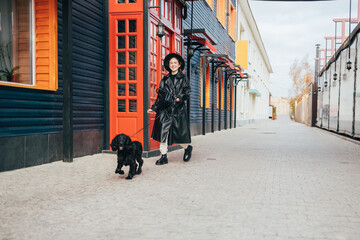 Happy stylish young woman walks her dog black cocker spaniel