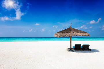 Two sunbeds under a parasol on a tropical paradise beach with blue sky, turquoise sea and copy space