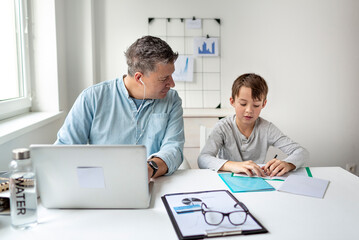 Business man works from home doing homeoffice and his son has homeschooling during corona crisis