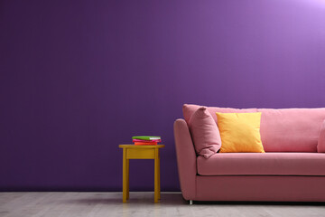 Comfortable pink sofa near purple wall in living room interior