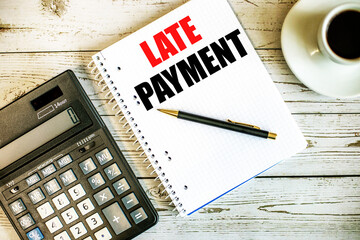 LATE PAYMENT written on white paper near coffee and calculator on a light wooden table. Business...