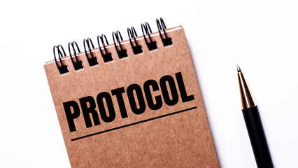 On a light background, a black pen and a brown notebook on black springs with the inscription...