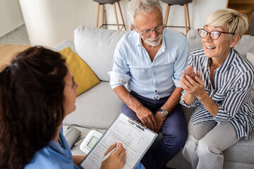 Female nurse talking to seniors patients being in a home visit, senior couple signs an insurance policy.