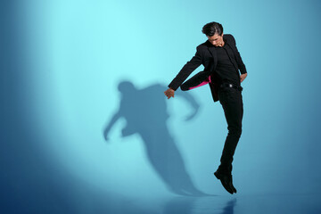 Fototapeta na wymiar Handsome young man in black stylish suit, jumping isolated on blue background. Horizontal view.