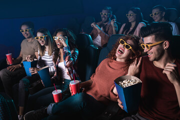 Group of cheerful people laughing while watching movie in cinema with 3D glasses.