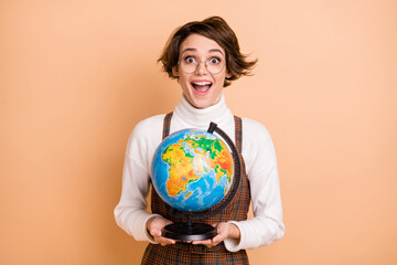 Photo of young attractive beautiful positive excited amazed girl in glasses hold globe isolated on beige color background