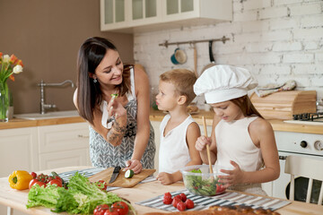 Family prepares lunch in the kitchen. Mom teaches her daughter and son to prepare a Salad of fresh vegetables. Healthy natural food, vitamins for children