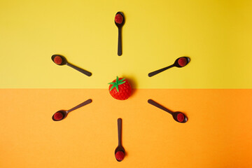 Squishy strawberry placed central on split of yellow and orange background. Flat lay arrangement of six chocolate spoons with fresh fruit -raspberries.