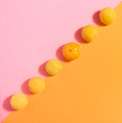 Combination of fresh organic apricot fruit and a tangerine lined in diagonal against pastel pink and orange flat lay.
