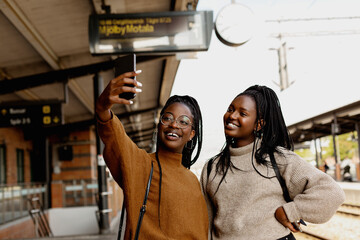 Smiling female friends taking selfie at train station platform