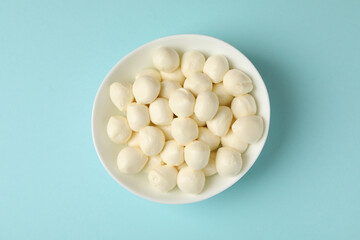 Bowl with fresh mozzarella cheese on blue background