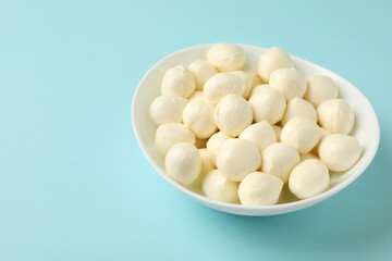 Bowl with fresh mozzarella cheese on blue background
