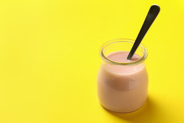 Glass jar with spoon and yogurt on yellow background