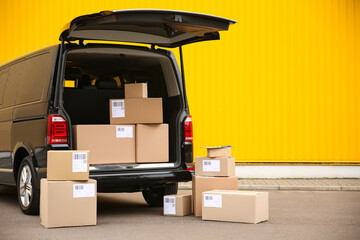 Black delivery van and many different parcels near yellow wall outdoors, space for text. Courier...
