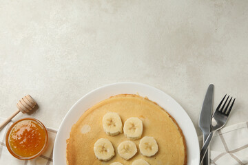 Concept of breakfast with plate of thin pancakes with banana, and jam on white textured background