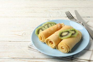Concept of breakfast with plate of crepes rolls with kiwi slices on wooden table