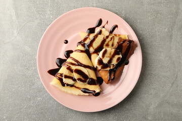 Plate of crepes with chocolate sauce and banana slices on gray background