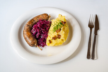 Baked bright pudding sausage with red cabbage and mashed potato on white plate.