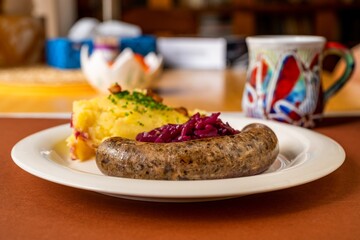 Baked bright pudding sausage with mashed potato and red cabbage on dining table.
