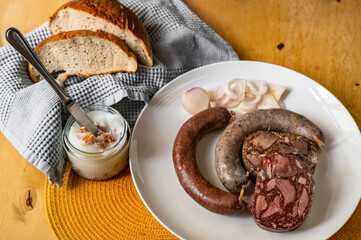 Bright and black pudding, sausage on plate, lard and greaves, bread and towel on table.