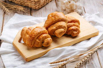 Three french croissants on the wooden cutting board decorated with wheat and napkin