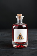 Glass bottle of poison with warning sign on black wooden table
