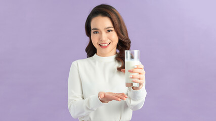 Cute healthy woman is drinking milk from a glass isolated on lilac background.