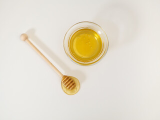 Natural flower honey from an apiary with a transparent bowl and a honey dipper on a white background. Flat lay, top view