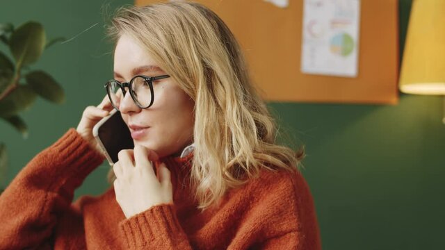 Chest up shot of young attractive businesswoman in casualwear and glasses chatting on mobile phone and smiling in the officeChest up shot of young attractive businesswoman in casualwear and glasses ch
