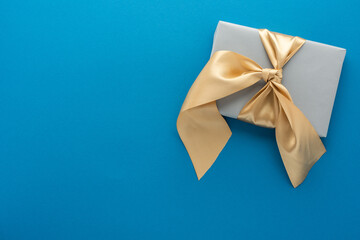 Gray gift box with golden bow on a blue background, birthday or valentine concept, top view, copy space