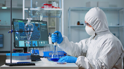 Chemist wearing ppe suit putting liquid in test tube with micropipette in laboratory. Team of doctors examining vaccine evolution using high tech and chemistry tools for virus development research