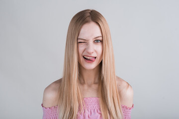 Fototapeta premium Young blonde girl makes funny grimaces in the studio on a white background