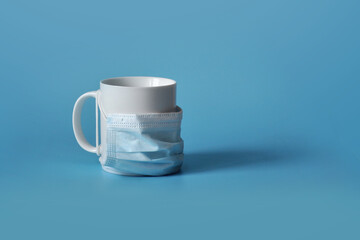 A white mug in a medical mask. A symbol of protection against viruses and infections,...
