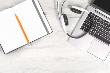 Laptop. keyboard and headphones on grey desk. pencil over notebook. Helpdesk or call center...